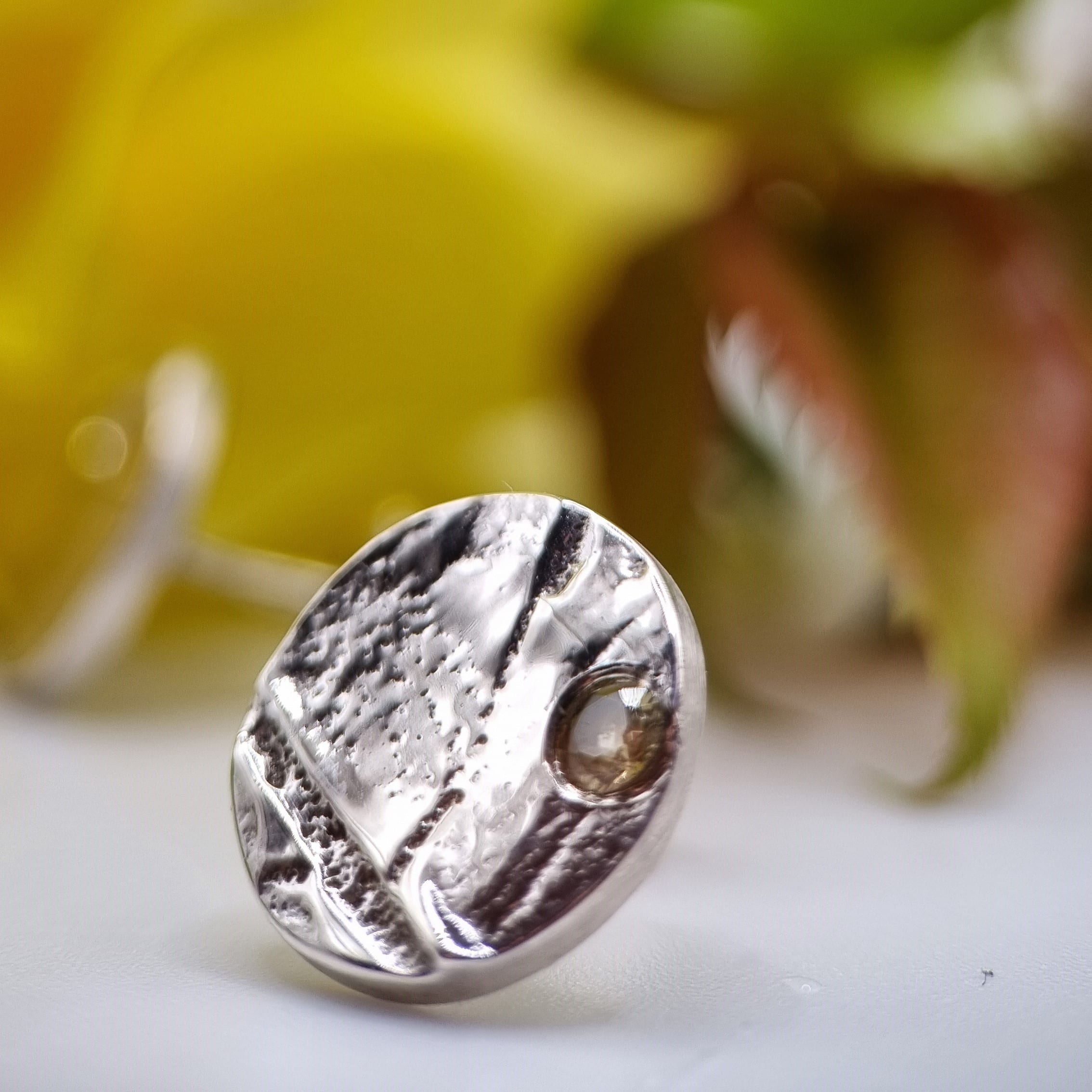 Photo d'une boucle d'oreille ronde, en argent 925 dans laquelle est serti un saphir jaune, avec en fond effet boken une rose jaune